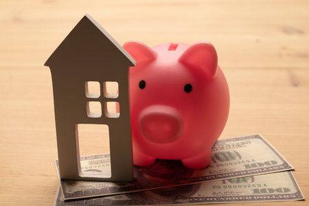Buy or rent concept. Toy house and piggy bank with dollar cash on wooden backgroundの写真素材
