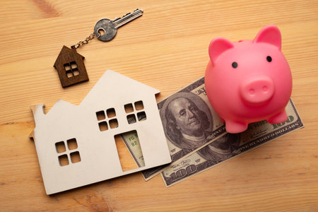 Buy Or Rent concept. Keys with trinket in shape of house and piggy bank with dollar cash on wooden background, top viewの写真素材