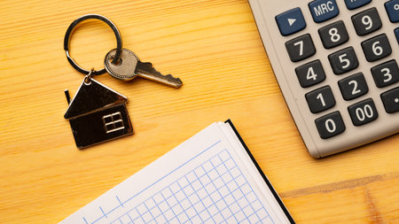 Buy or rent concept. Keys with trinket in shape of house and notepad with calculatoron on wooden background, top viewの写真素材