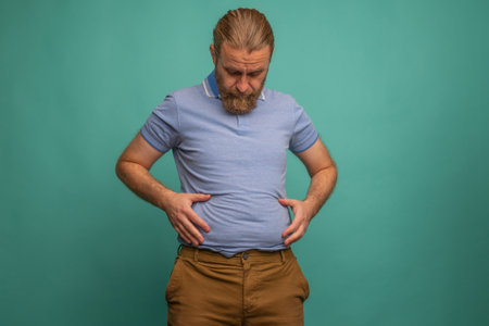 A man with a sad face feels his fat belly on blue background, closeup. Space for textの写真素材