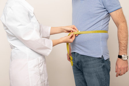 Nutritionist measuring overweight man's waist with tape in clinic, closeupの写真素材