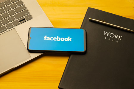 Kyoto city, Japan - July 31, 2023: Facebook logo on the smartphone screen is placed on the Apple macbook keyboard on wooden desk background.のeditorial素材