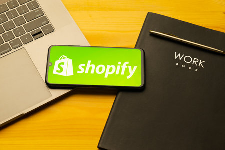 Kyoto city, Japan - July 31, 2023: Apple iPhone with Shopify logo on the screen on wooden backgroundのeditorial素材