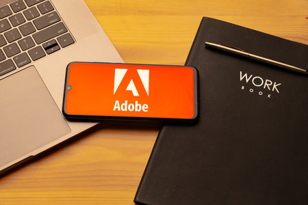 Kyoto city, Japan - July 31, 2023: Adobe logo on the smartphone screen is placed on the Apple macbook keyboard on wooden desk background.のeditorial素材