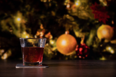 Glass of whiskey on the bar in front of the blur image Christmas home room with tree and festive bokeh lighting, blurred holiday backgroundの写真素材