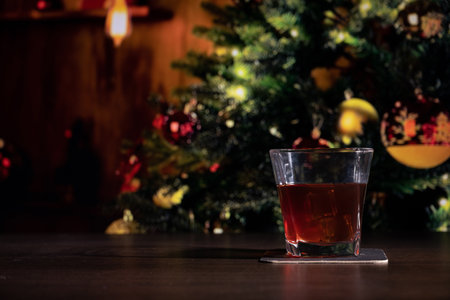 Glass of whiskey on the bar in front of the blur image Christmas home room with tree and festive bokeh lighting, blurred holiday backgroundの写真素材