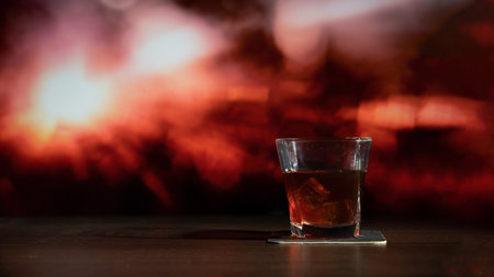 Glass of whiskey on the bar in front of the blur image Abstract Natural Sun flare on the blackの写真素材