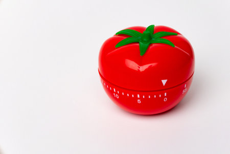 Close up view of mechanical tomato shaped kitchen clock timer for cooking and studying. Used for pomodoro technique for time & productivity management. Isolated on white background, set at 5 minutes.の写真素材