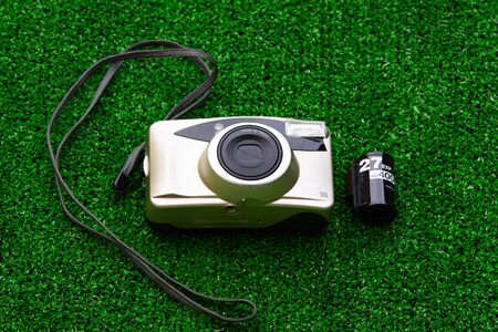 Old film camera with 35mm film cartridge isolated on green grass background.