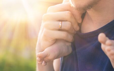 Man's hand with a wedding ring on his finger, holding the foot of his bare little child. Toddler is sitting at his father's neck on the background of soft sunlight and blurred green bokehの写真素材