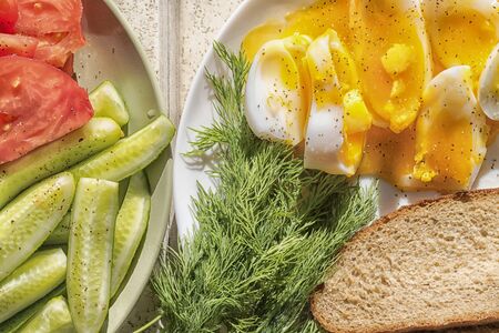 Sliced egg with soft yolk, vegetables, cucumbers, tomatoes and dill with a piece of brown bread....