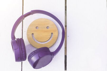 Fine music for perfect mood. Wireless purple headphones and a wooden smile on a white background. New technologies. Modern technology. Copyspace.の写真素材