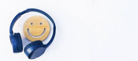 Fine music for perfect mood. Wireless headphones of color classic blue on a white background. A wooden smile. Concept of love for music. Nobody. Copyspace banner.の写真素材