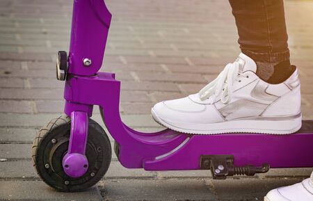 Leg in white sneaker set on a purple pink electric scooter. Close-up. Side view. Ecotransportの写真素材