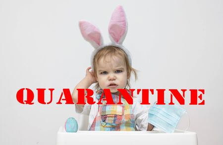 Angry toddler child kid with easter bunny ears holds a medical mask. Easter and quarantine concept...
