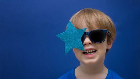 happy blond boy with glasses star looks up into the camera smiling on a dark blue backgroundの写真素材