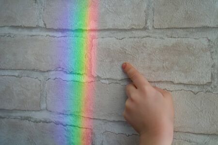 A real rainbow on the wall of brick wallpaper. Child's hand wants to touch rainbow light reflection.の写真素材
