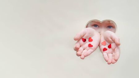 Hands and face of a baby from a hole in the shape of a heart. Childrens hands hold out hearts and give love. Unconditional love and affection, concept of childrens love, mothers day, adopted child.の写真素材