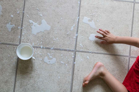 Childs bare feet standing in puddle of spilled milk on floor with white cupの写真素材