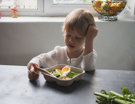 Sad child boy sadly picks a plate of healthy food with a spoon. Difficulty feeding children. The...