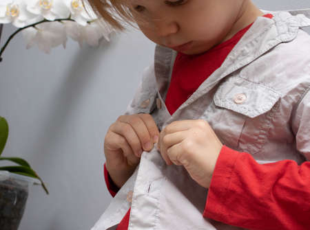 Childhood independence concept ,little boy buttoning on shirt, fastening his buttons , on white gray...