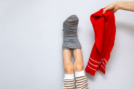 Childrens feet in one woolen sock. The legs are frozen, my mothers concern is to dress the child. Heating, cooling, autumn concept on gray background copy space. Mother tied son with her careの写真素材