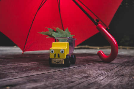toy car truck hiding from the rain under an umbrella with a positive smile. Concept of autumn and...