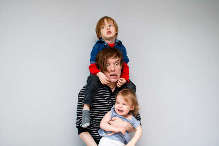 A young father holds two children on himself and screams insanely emotionally in panic under the pressure of responsibility and fatigue from children.の写真素材