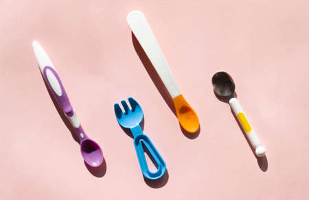 Colorful eating utensils. Different spoons for starting baby foods. Choosing a spoon or fork for your baby. Top view of flat lay on pink backgroundの写真素材
