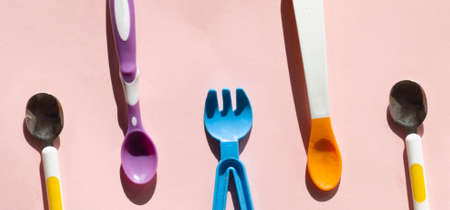Colorful eating utensils. Different spoons for starting baby foods. Choosing a spoon or fork for your baby. Top view of flat lay on pink backgroundの写真素材