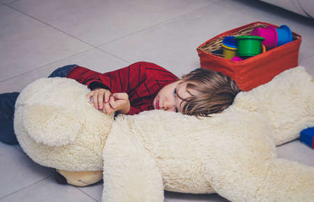 Unhappy Child boy lies on the floor at home or in kindergarten among toys and is sad or falls asleep. Social concept of childhood loneliness, illness and sadness. Adaptation to kindergartenの写真素材