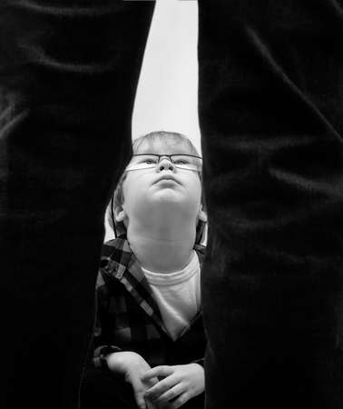 A little boy with glasses is sitting and looking up at the standing man in dismay. Domestic...