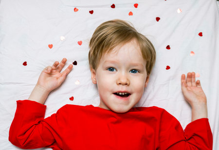 A kid todder child lies on a bed with hearts. Concept of first love and valentines in kindergarten and schoolの写真素材