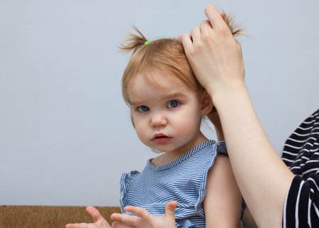 A young father combs the hair of a little girl daughter with a wooden eco-friendly comb and does a ponytail hairstyle in front of the kindergarten in the morningの写真素材