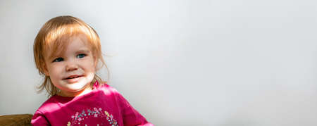 Portrait of a little toddler girl caught in the suns rays. Girl smiling looking to the side on a gray neutral background with place for text. Bannerの写真素材