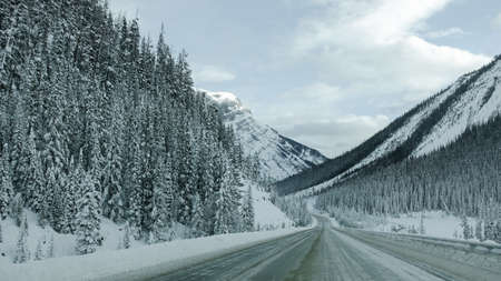 Snow-capped mountains with a frozen waterfall along Trans-Canada Highway in Banff National Park in Alberta, Canadaの写真素材