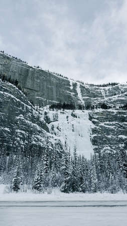 Snow-capped mountains with a frozen waterfall along Trans-Canada Highway in Banff National Park in Alberta, Canadaの写真素材