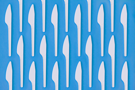 Flay lay photo of white plastic disposable knives. Creative top view pattern. Calm clear colours.