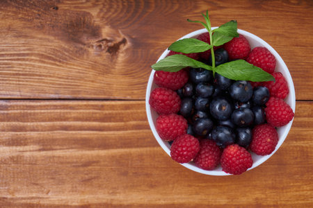 blueberries and raspberries in a white bowl over a wooden table. a delicious idea for a healthy breakfast or snack.の写真素材