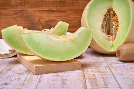green melon sliced on wooden board with kiwis and a half melon. over a wooden table and wooden background. healthy food concept. Summer fruitの写真素材