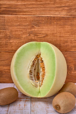 green melon sliced on wooden board with kiwis and a half melon. over a wooden table and wooden background. healthy food concept. Summer fruitの写真素材