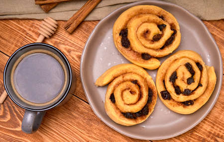 cinnamon rolls with raisins on brown plate and a cup of coffee for breakfast. in the background a...