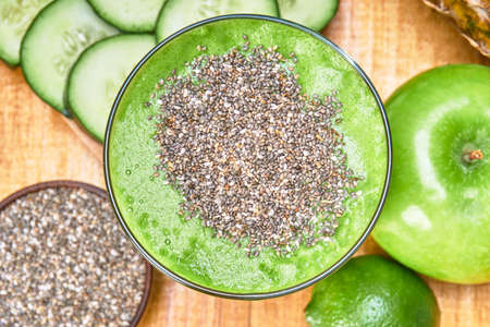 green smoothie of spinach, cucumber, lemon, and pineapple. fresh fruit on the side and a wooden bowl with chia seeds. wooden table with wooden planks and white wooden background. top viewの写真素材