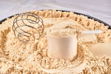 vanilla whey protein scoop on a mountain of protein powder on a marble surface. copy space for...