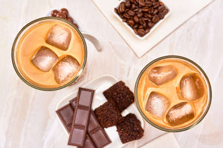 iced latte accompanied by chocolate pearls, vegan brownies and chocolate bars on a marble surface. luxury concept. copy space for advertising. top view.の写真素材