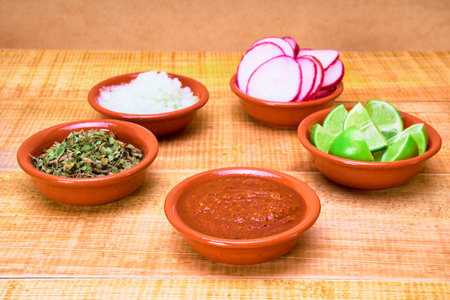 condiments to accompany the pozole such as oregano, onion, sliced radishes, lime and salsa on clay plates on a wooden surface and wooden background with copy space for advertising.の写真素材