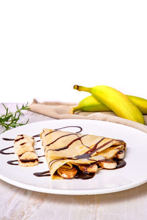 french crepes with chocolate syrup and banana on a white plate on a marble surface. copy space for advertising, elegant concept.の写真素材