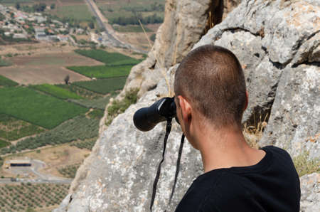 the guy looks through binoculars into the mountain peaks downの写真素材