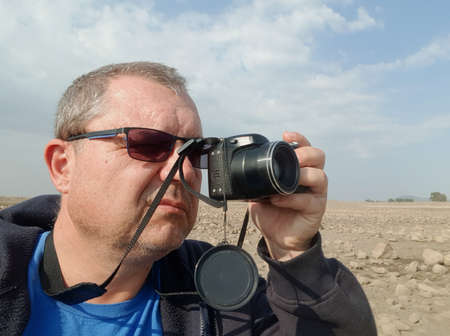 a man in sunglasses holds a camera with one hand and photographs the landscape of a rocky plainの写真素材