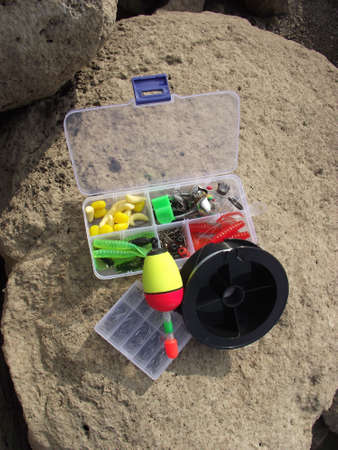 on the rocky shore on one of the large stones fishing tackle is randomly lying in the background the water of the lake is visible.の写真素材